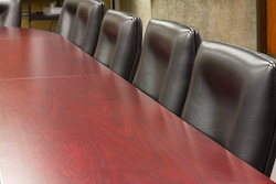 Black office chairs lined up against a wooden conference table.