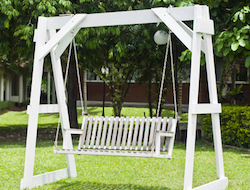 A photo of a white stand-alone swing on a grassy field with trees and bushes in the background