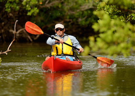 Photo of a man wearing a yellow life jacket riding a red kayak down a river